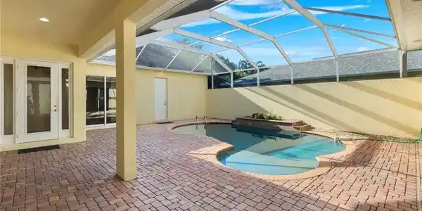Image 4: Screened lanai featuring a freeform swimming pool with integrated spa, pavers, and multiple access points to the interior