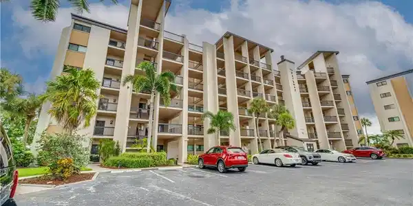 Image 3: Multi-story building featuring multiple private balconies, a paved parking area, and mature palm trees