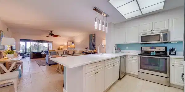Image 4: White cabinetry with stainless steel appliances, white countertops, modern pendant lighting, and tiled flooring