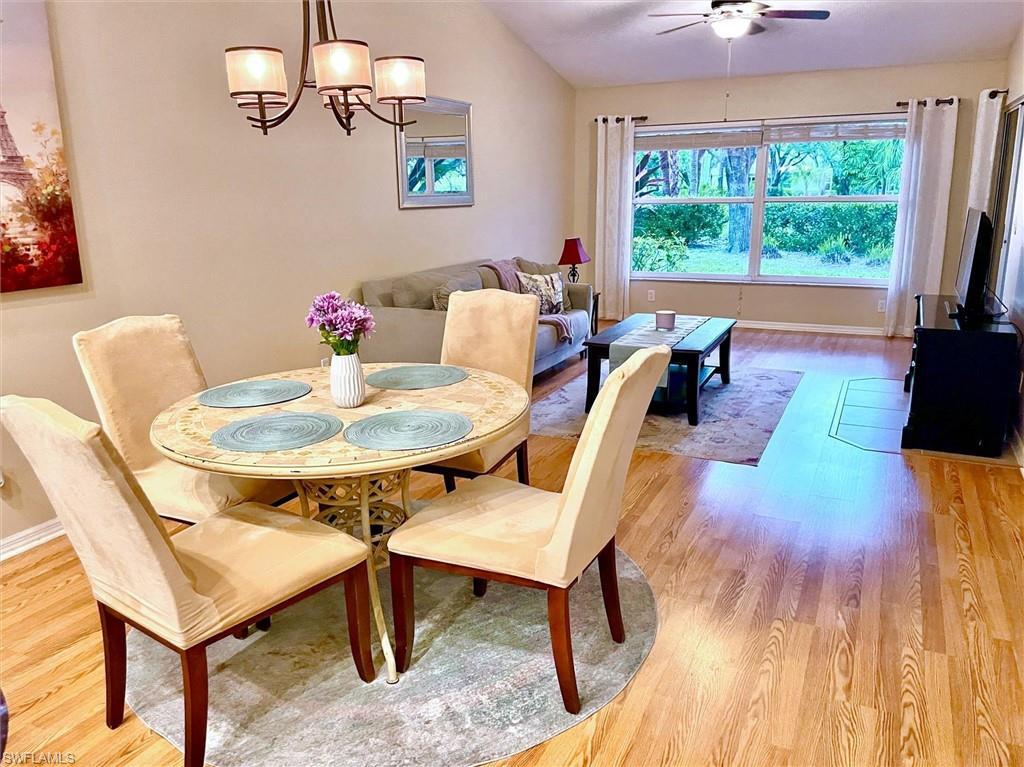 Image 4: Open-concept living and dining area featuring wood-finish flooring, a vaulted ceiling, a large picture window, and a ceiling fan