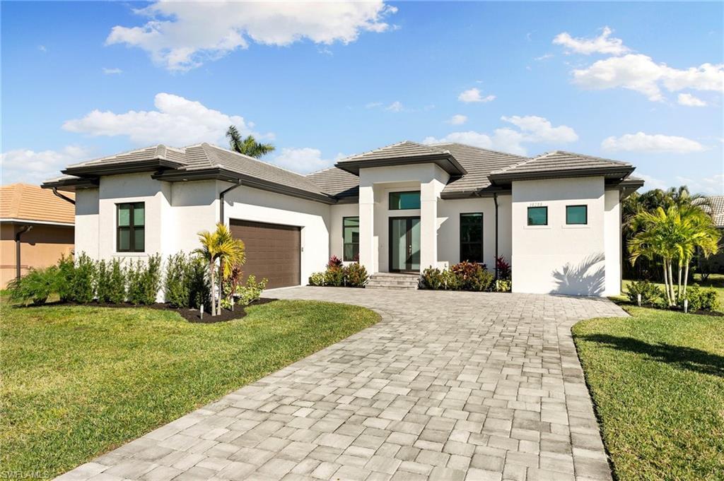 Image 1: Prairie-style home with a garage, decorative driveway, stucco siding, and a front lawn