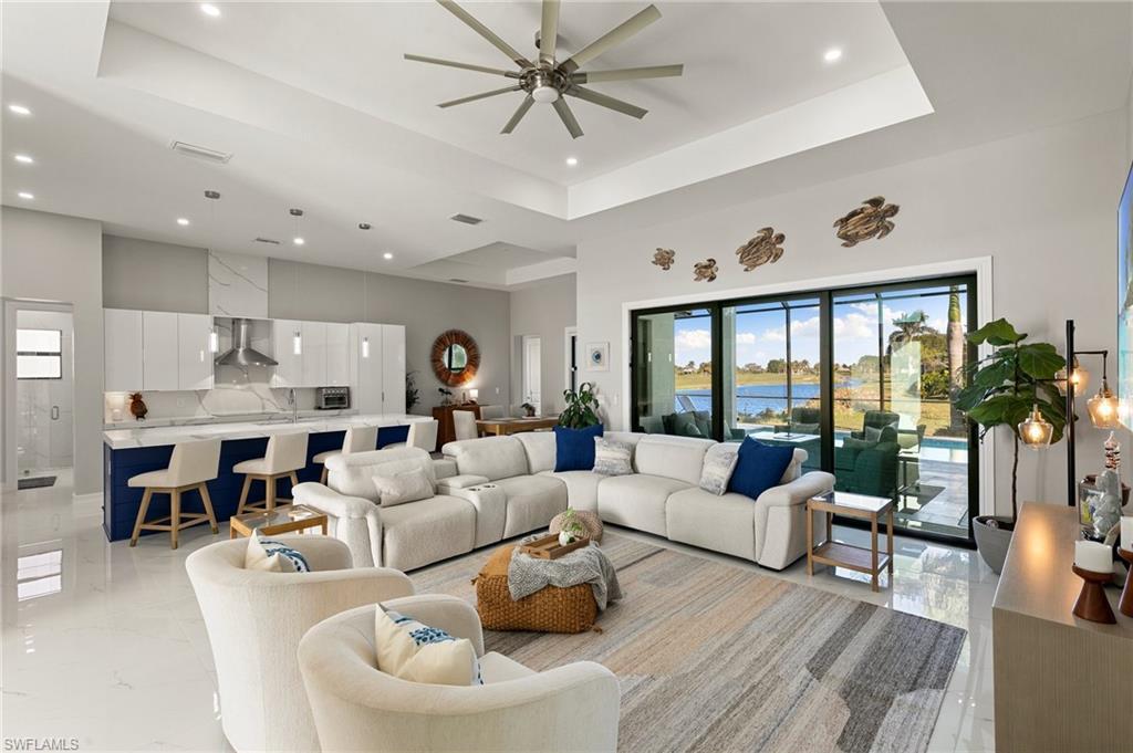 Image 4: Living room featuring a tray ceiling, a water view, a ceiling fan, a towering ceiling, and recessed lighting
