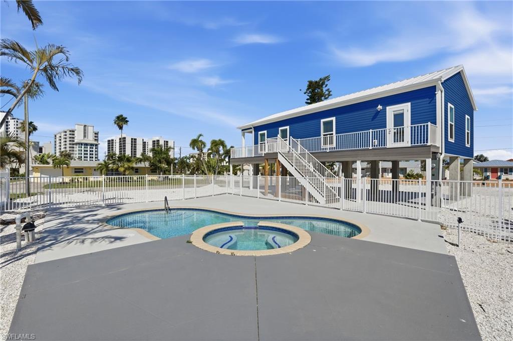 Image 2: Elevated coastal property featuring a blue exterior with white trim, a multi-tiered pool and spa, and a surrounding privacy fence - Virtually Edited Image