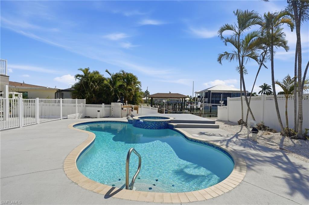 Image 4: Resort-style pool area featuring a freeform swimming pool with integrated spa, surrounding concrete patio, and white privacy fencing - Virtually Edited Image