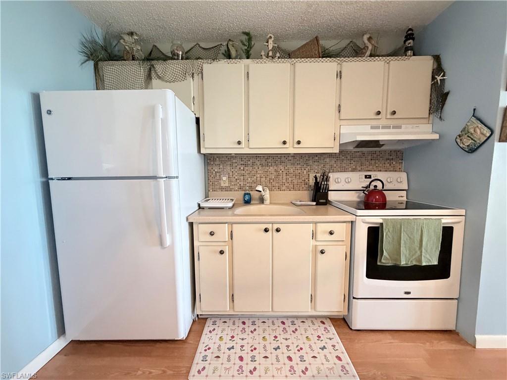 Image 4: Kitchen featuring white appliances, light countertops, decorative backsplash, under cabinet range hood, and light wood finished floors