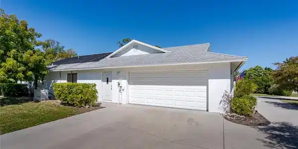 Image 3: View of front facade of large garage with circular driveway, a shingled roof, solar panels.