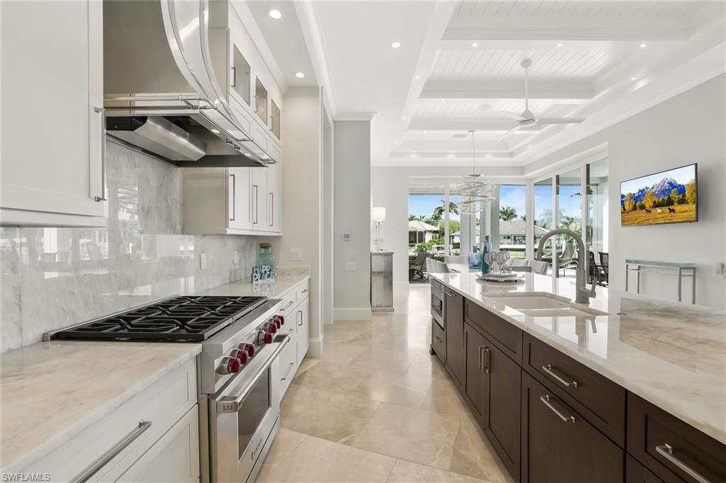 Image 2: Kitchen featuring stainless steel appliances, light stone countertops, two tone cabinetry, glass fronted cabinets, and decorative light fixtures