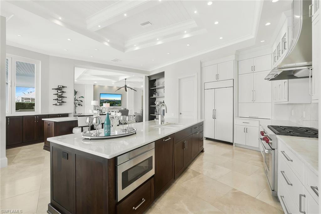 Image 4: Kitchen featuring ornamental molding, light stone countertops, built in appliances, ventilation hood, and glass fronted cabinets