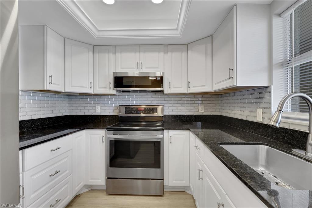 Image 2: Updated Kitchen with Stainless Steel Appliances, White Cabinetry, Dark Stone Countertops and Light Wood Flooring