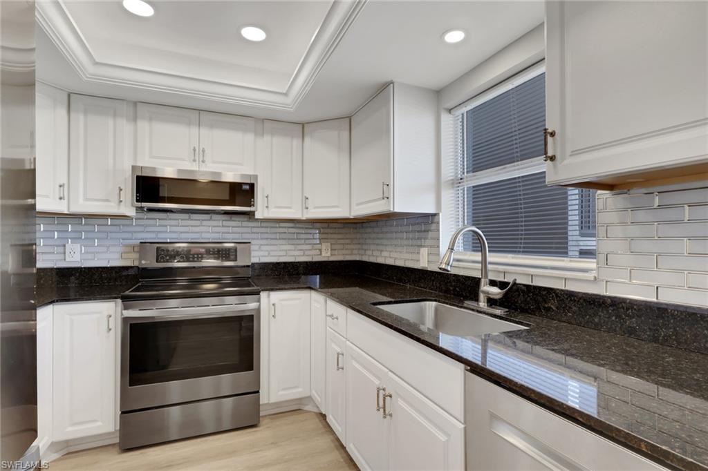 Image 3: Updated Kitchen with Stainless Steel Appliances, White Cabinetry, Dark Stone Countertops and Light Wood Flooring