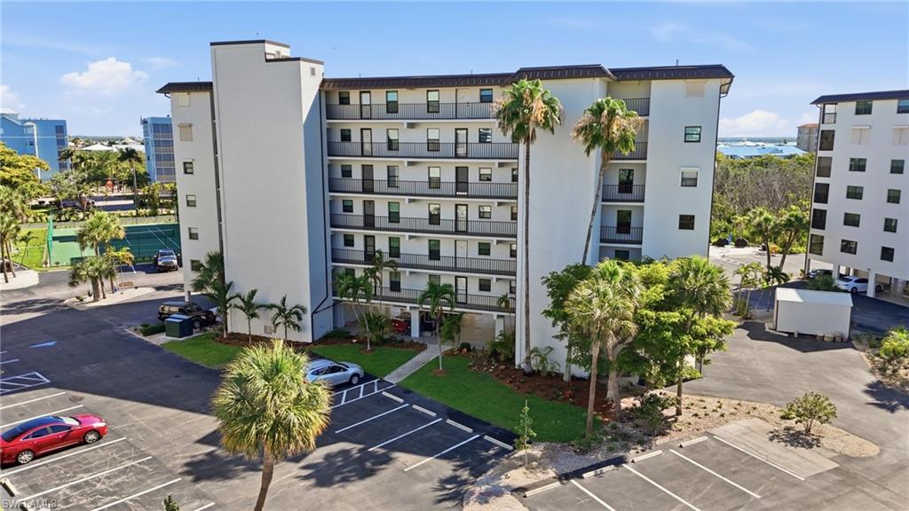 Image 2: Modern multi-story building featuring individual balconies, a large parking area, and mature palm trees - Virtually Edited Image