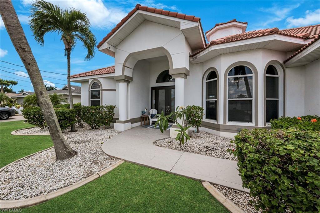 Image 2: Exterior featuring a white stucco facade, a red tile roof, arched windows, a curved concrete walkway, and landscaped garden beds with white stone