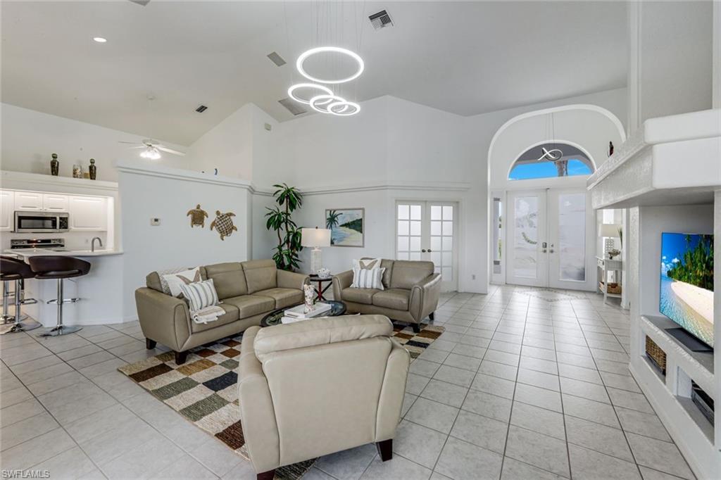 Image 4: Spacious living area featuring vaulted ceilings, contemporary circular pendant lighting, and light-toned tile flooring
