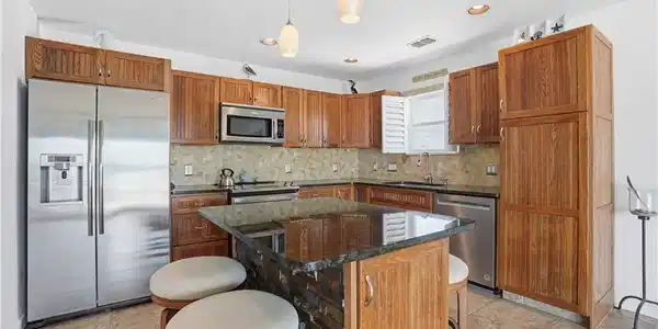 Image 4: Kitchen featuring wood cabinetry, stainless steel appliances, a stone tile backsplash, a dark countertop island with stone detailing, and recessed lighting