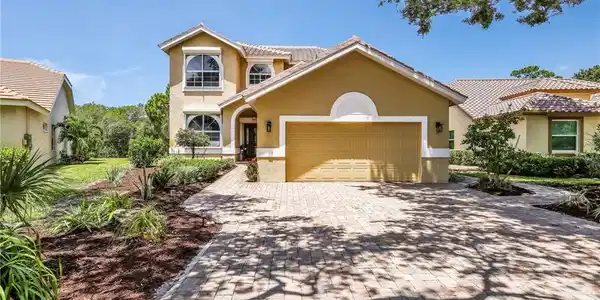 Image 3: Stucco exterior with a tiled roof, paver driveway, arched entryway, and landscaped garden beds