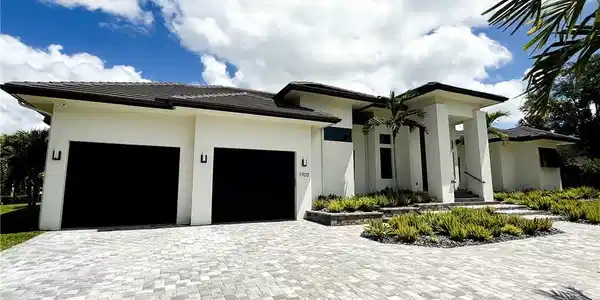 Image 3: Contemporary residence featuring a paver driveway, two-car garage, and a covered entry with columns
