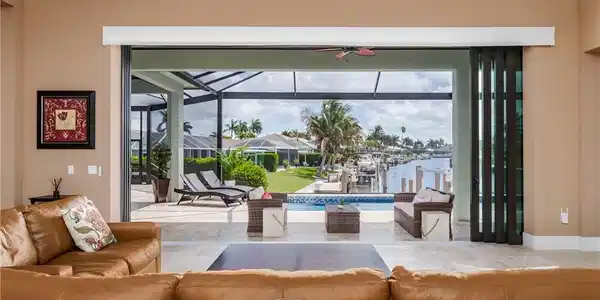 Image 4: Expansive folding glass doors open to a screened lanai with a swimming pool, extending to a waterfront canal