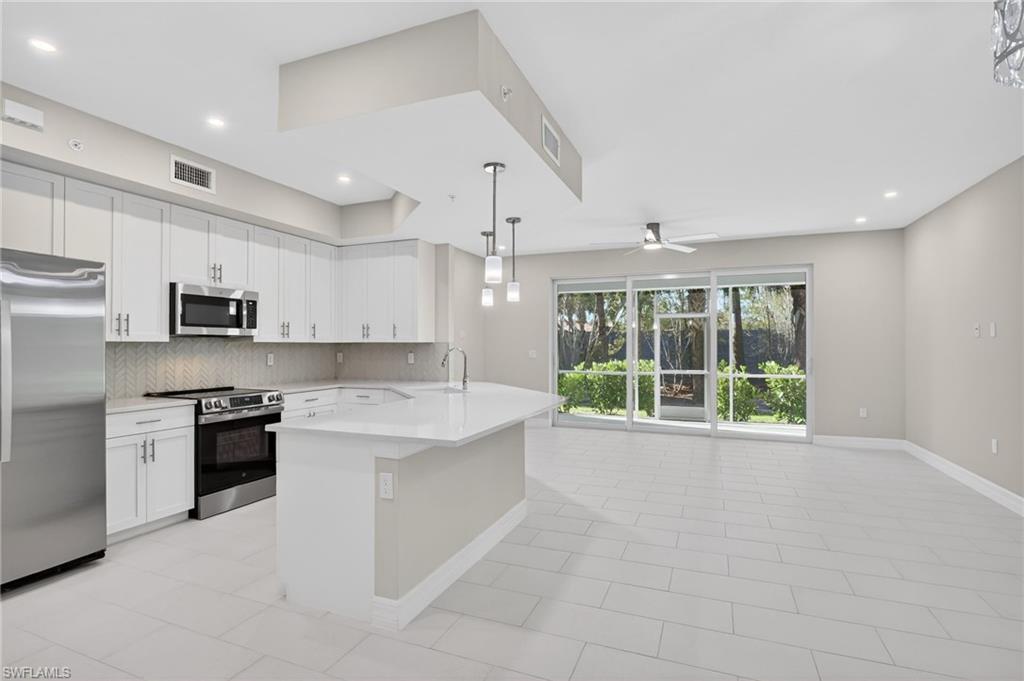 Image 2: Open-concept kitchen and living area featuring a central island with pendant lighting, stainless steel appliances, white cabinetry, and wood-finish tile flooring