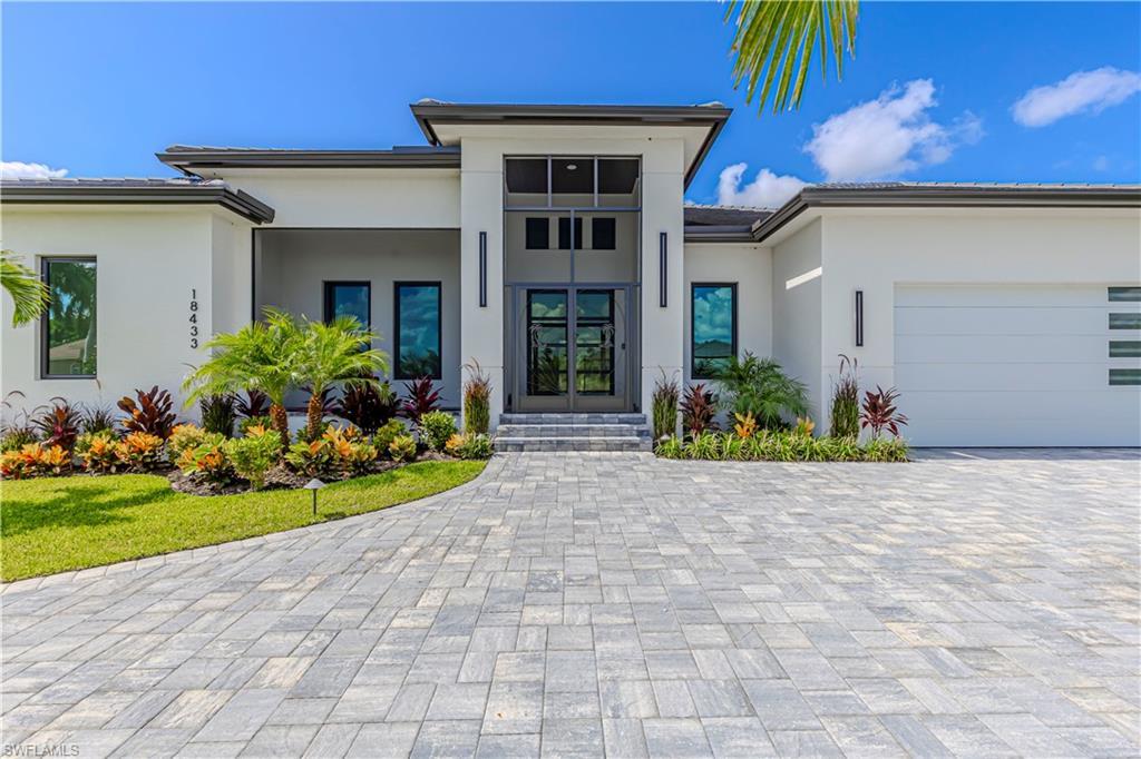 Image 2: Modern architectural facade featuring a prominent double-door entry with transom windows, a paver driveway, and an integrated garage