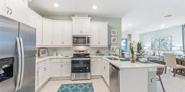 Image 4: Well-appointed kitchen featuring white cabinetry, stainless steel appliances, and light-colored countertops