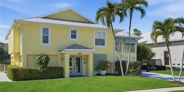 Image 4: Two-story residence featuring stucco exterior, light blue double-entry doors, a balcony with a white railing, and a metal roof