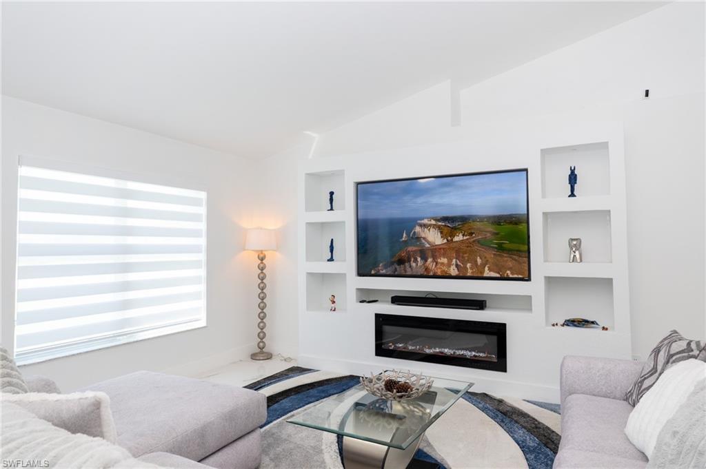 Image 3: Living room with a glass covered fireplace, vaulted ceiling, and built in features