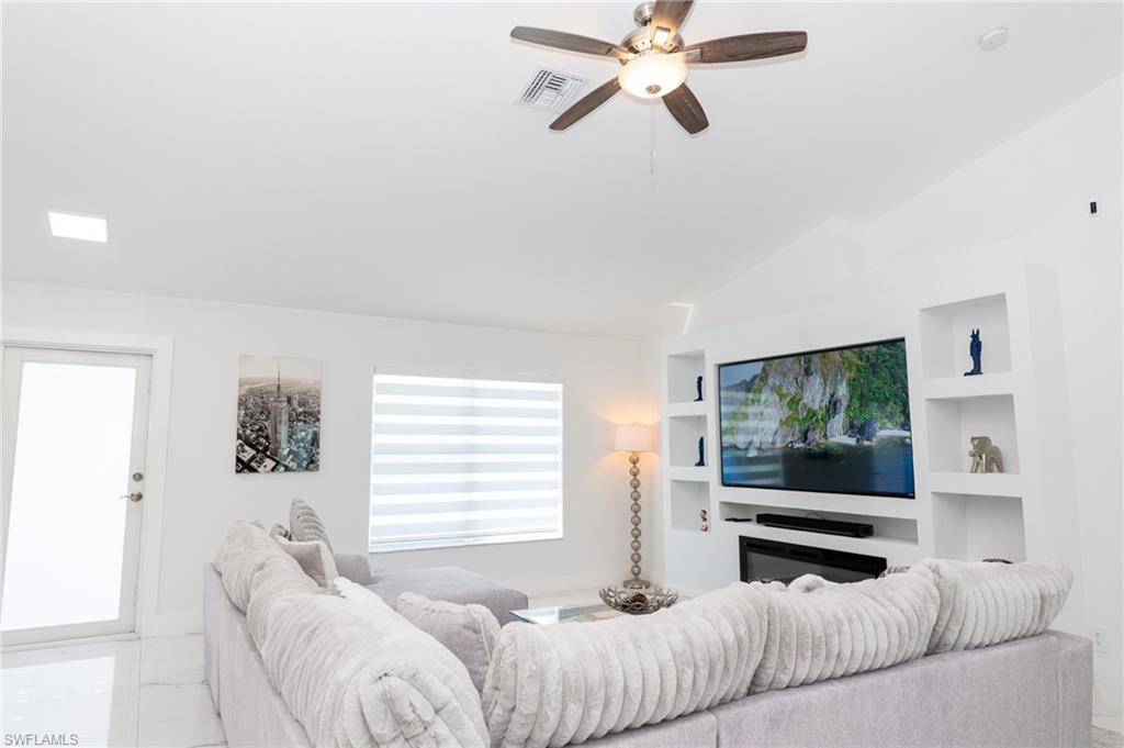 Image 4: Living room featuring lofted ceiling, a ceiling fan, built in features, and marble look tile flooring