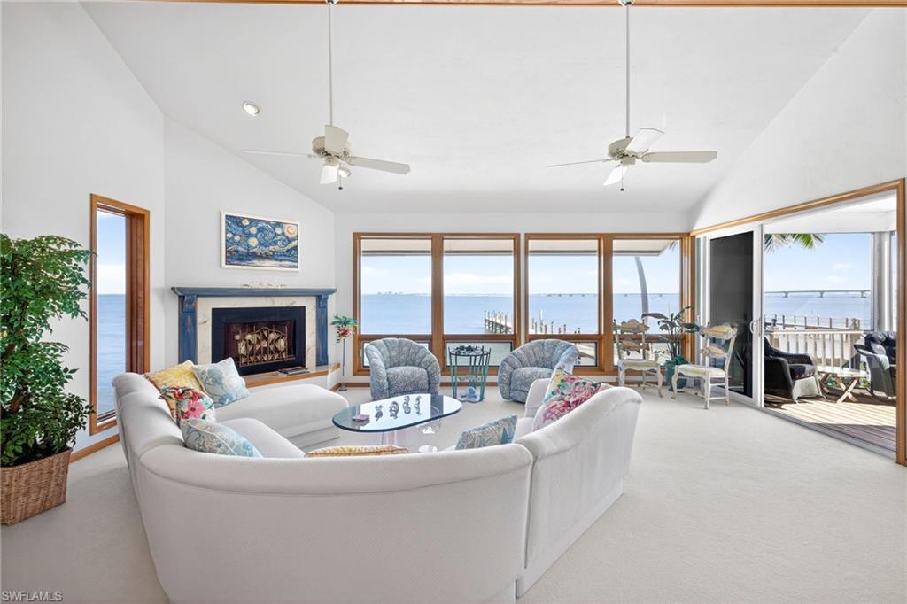 Image 4: Carpeted living room with a water view, high vaulted ceiling, plenty of natural light, a high end fireplace, and ceiling fan