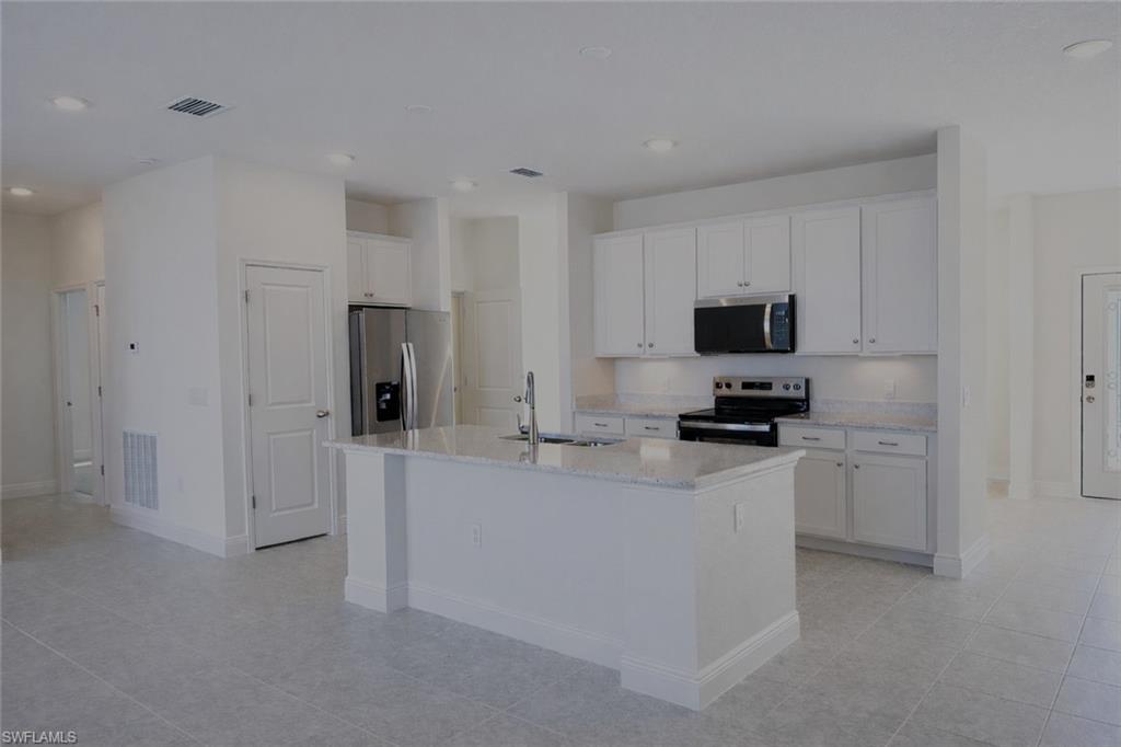 Image 2: Kitchen featuring stainless steel appliances, white cabinetry, an island with sink, light stone countertops, and recessed lighting