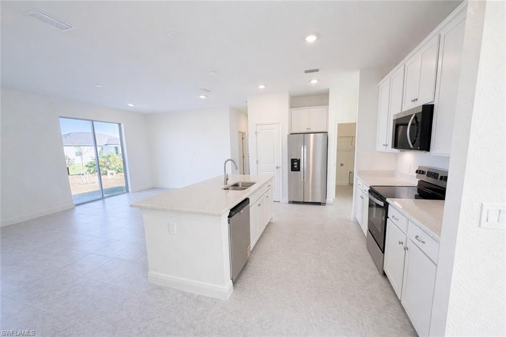 Image 3: Kitchen featuring stainless steel appliances, white cabinets, a center island with sink, recessed lighting, and open floor plan