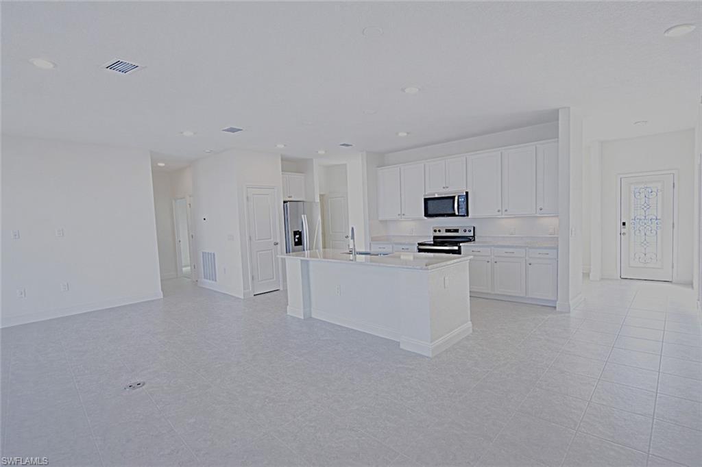 Image 4: Kitchen featuring white cabinetry, stainless steel appliances, a kitchen island with sink, recessed lighting, and light stone countertops