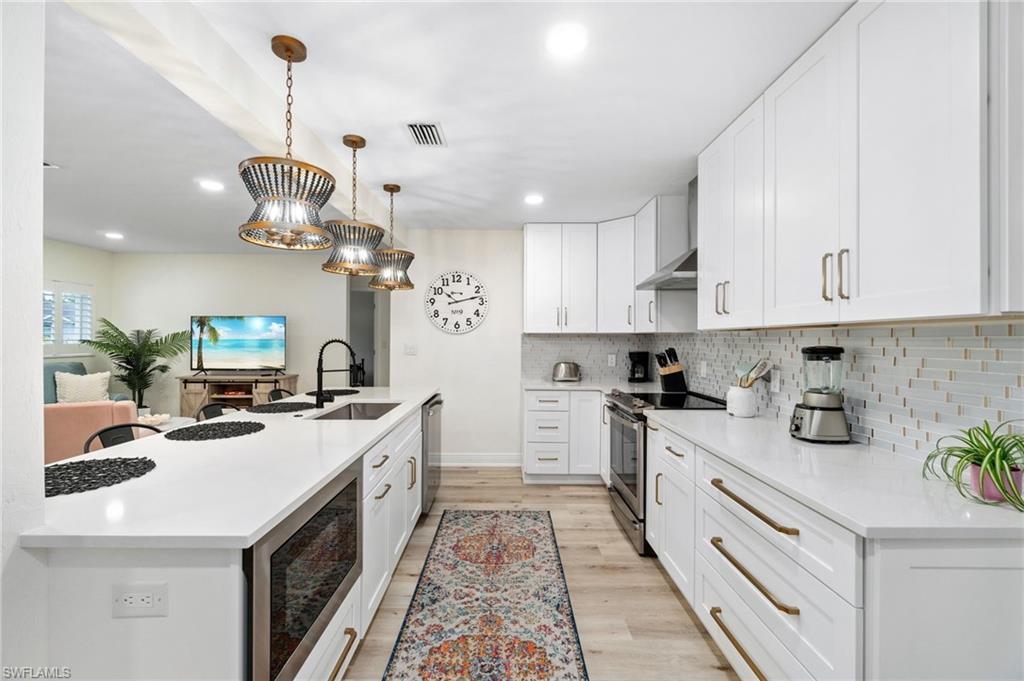 Image 2: Kitchen featuring stainless steel appliances, decorative light fixtures, white cabinetry, light stone counters, and light wood-style flooring