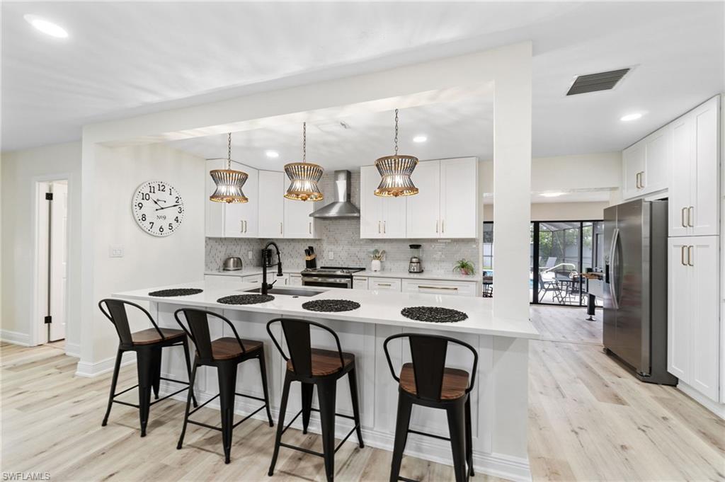 Image 4: Kitchen with decorative light fixtures, stainless steel appliances, white cabinets, a kitchen bar, and light wood-style floors