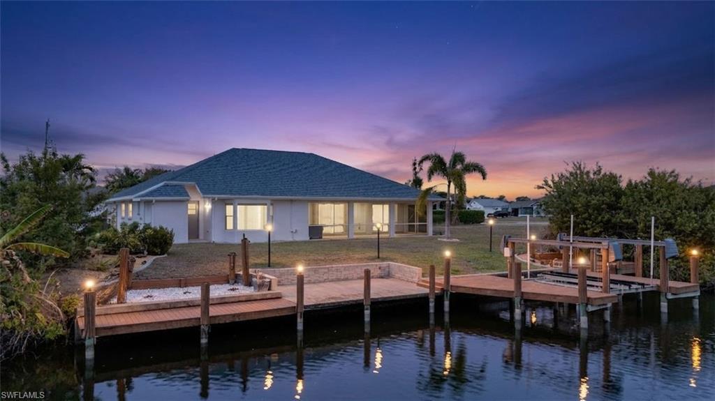 Image 1: Back of property at dusk with a water view, boat lift, and a shingled roof