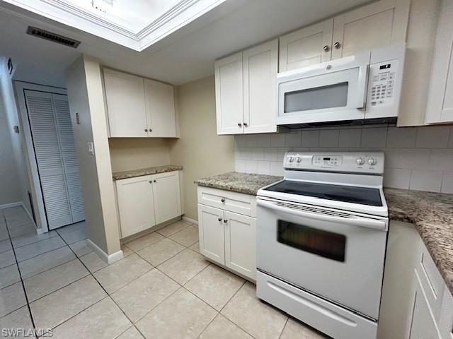 Image 4: Kitchen with white appliances, white cabinetry, light tile patterned flooring, backsplash, and light stone countertops