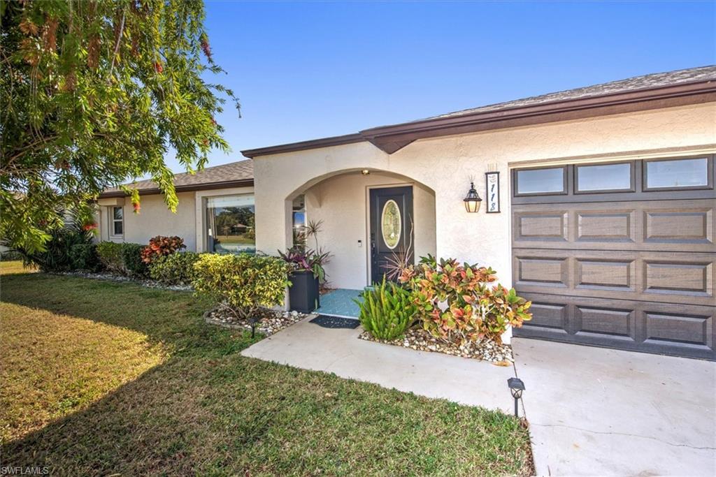 Image 2: Doorway to property featuring a garage, stucco siding, a lawn, and driveway