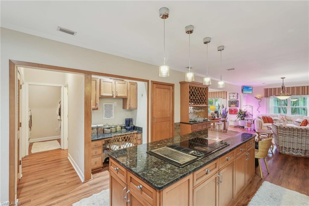 Image 4: Kitchen with light wood-style flooring, visible vents, a kitchen island, decorative light fixtures, and black electric stovetop