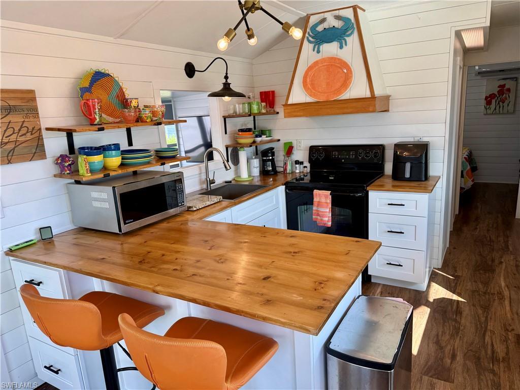 Image 2: Kitchen with butcher block countertops, white cabinets, wooden walls, stainless steel microwave, and dark wood-type flooring