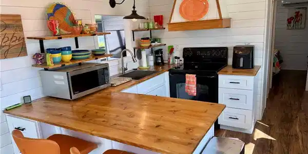 Image 2: Kitchen with butcher block countertops, white cabinets, wooden walls, stainless steel microwave, and dark wood-type flooring