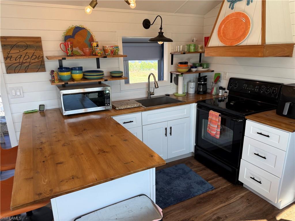 Image 4: Kitchen with butcher block counters, black range with electric cooktop, white cabinetry, extractor fan, and stainless steel microwave