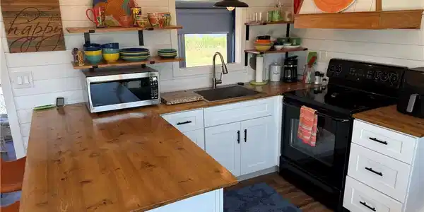 Image 4: Kitchen with butcher block counters, black range with electric cooktop, white cabinetry, extractor fan, and stainless steel microwave