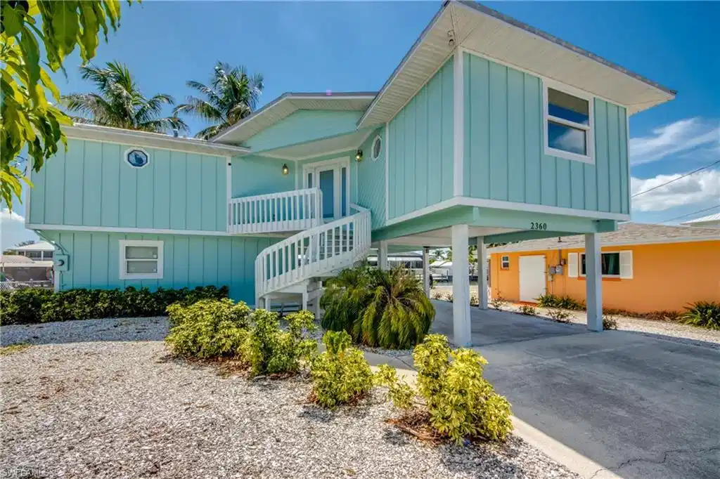 Image 1: Coastal-style elevated residence featuring turquoise vertical siding and white trim