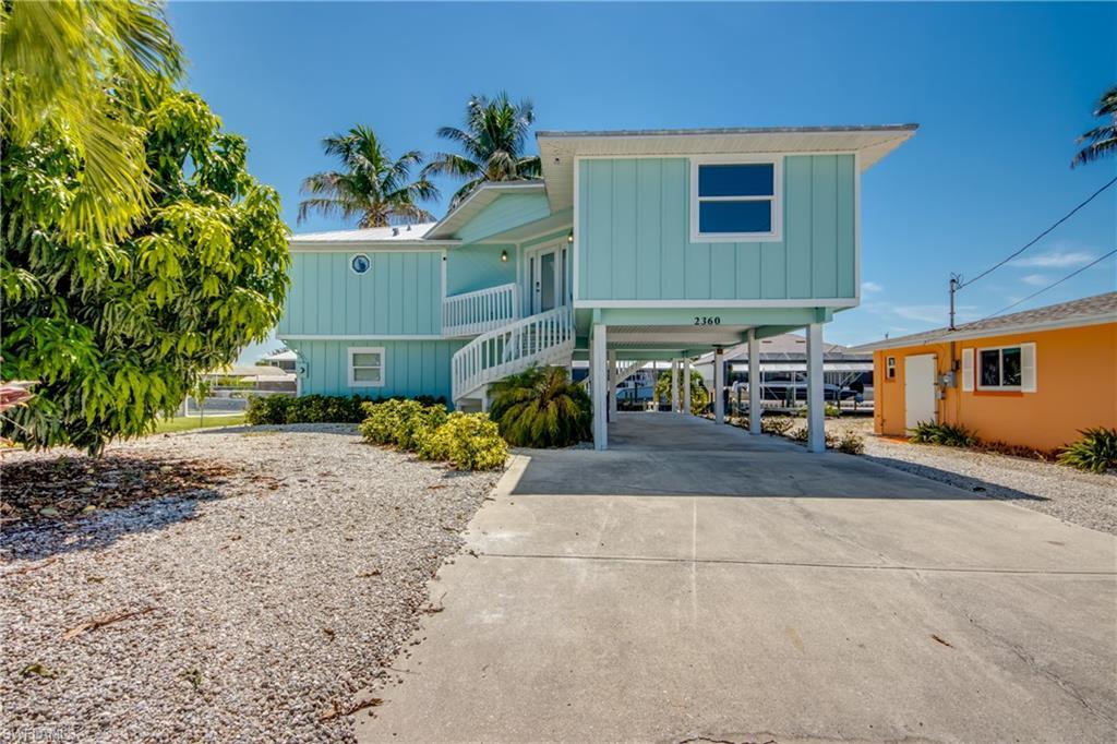 Image 2: Stilted coastal residence featuring light blue siding, a white spiral staircase, and a concrete driveway
