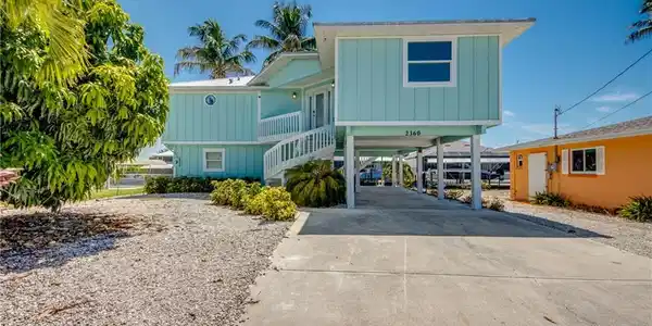 Image 2: Stilted coastal residence featuring light blue siding, a white spiral staircase, and a concrete driveway
