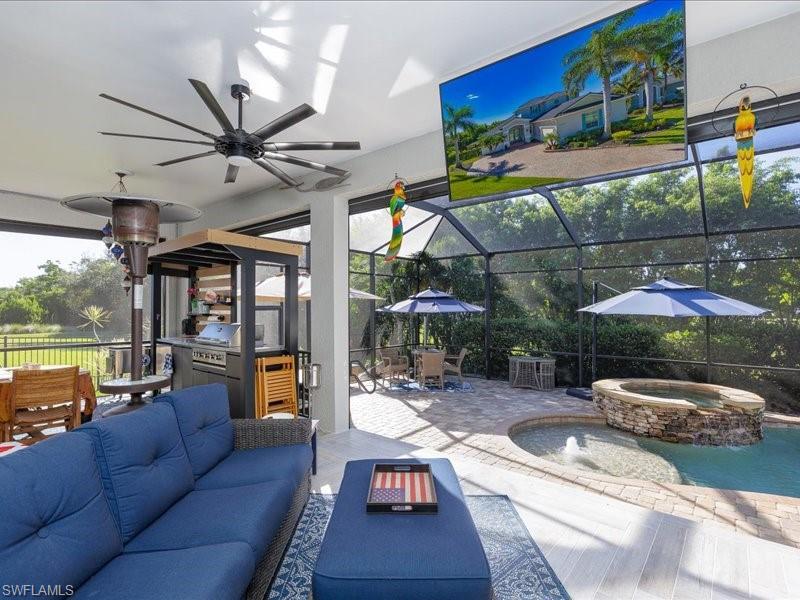 Image 1: Screened lanai featuring wood-finish flooring, a built-in outdoor kitchen, a large ceiling fan, and a stone-accented spa with water feature