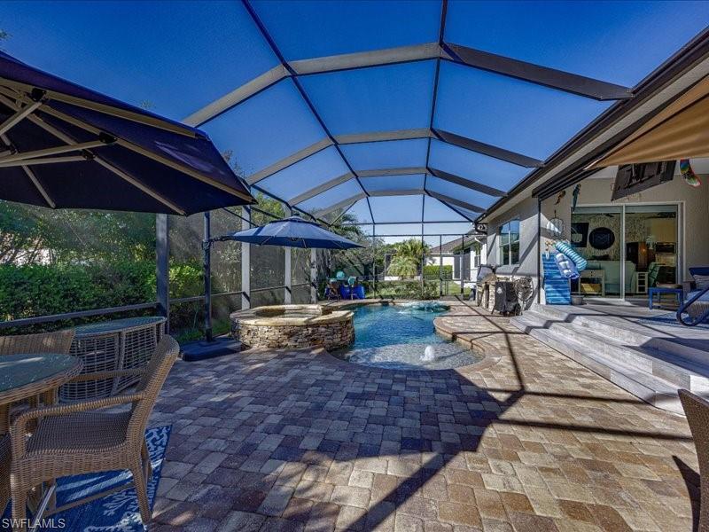 Image 3: Screened outdoor living area featuring a paver patio, integrated spa, and swimming pool with water features