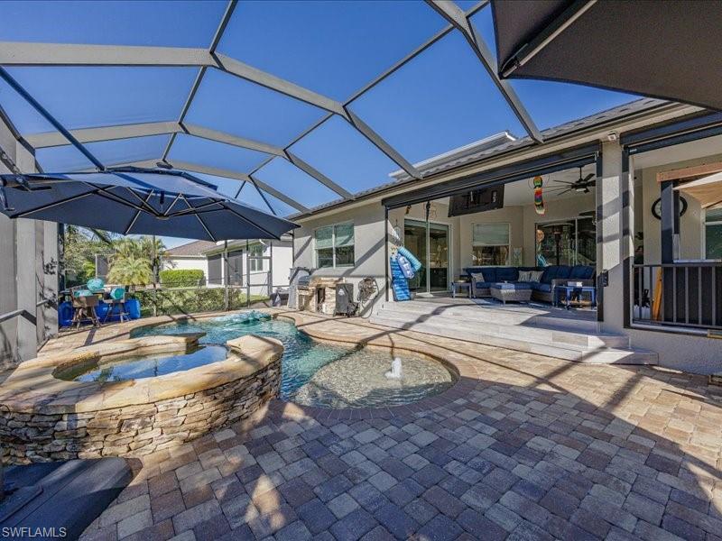 Image 4: Screened lanai featuring a paver patio, a stone-clad spa and pool with water features, an outdoor kitchen with built-in cabinetry, and a covered porch with sliding glass doors