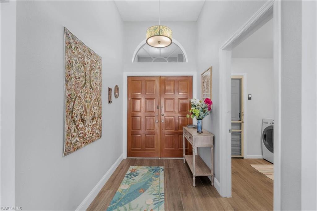 Image 3: Foyer featuring double entry doors with a transom window, high ceilings, wood-finish flooring, and a decorative drum pendant light fixture