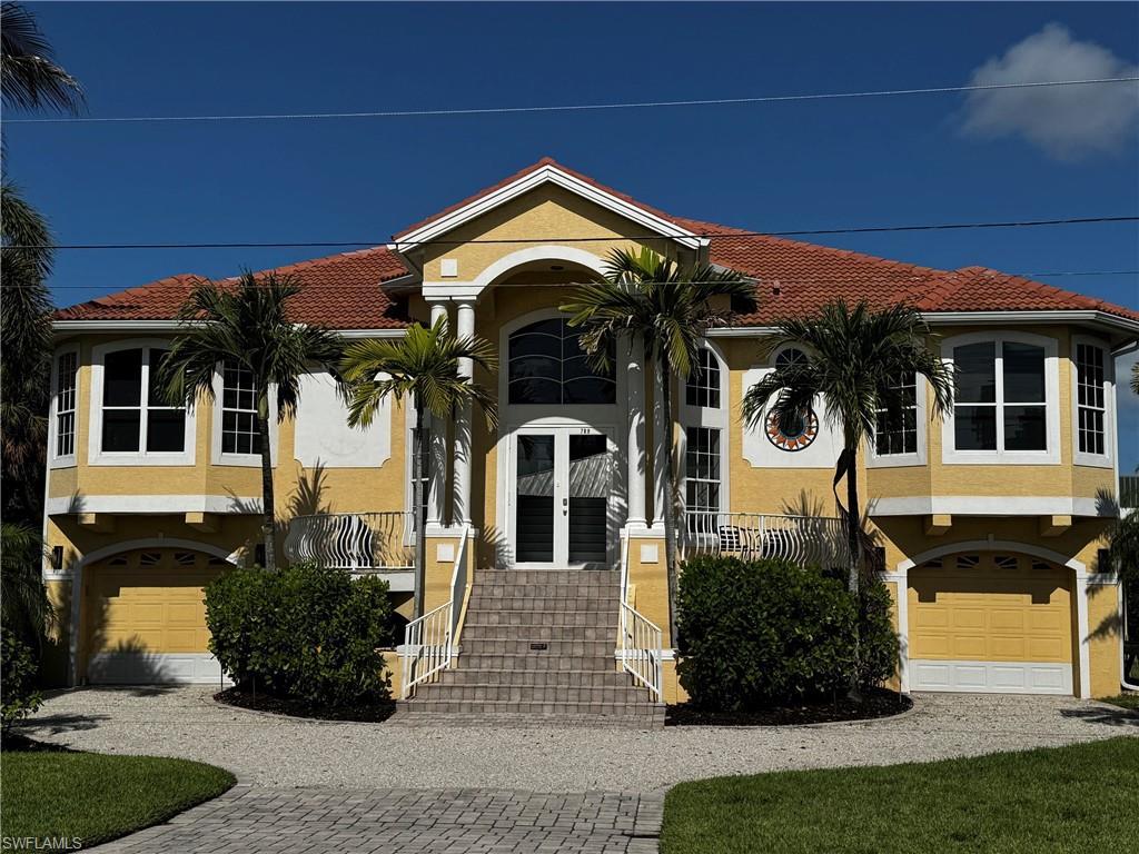 Image 1: Mediterranean-inspired stucco exterior featuring a terra cotta tile roof, prominent bay windows, and a paver driveway