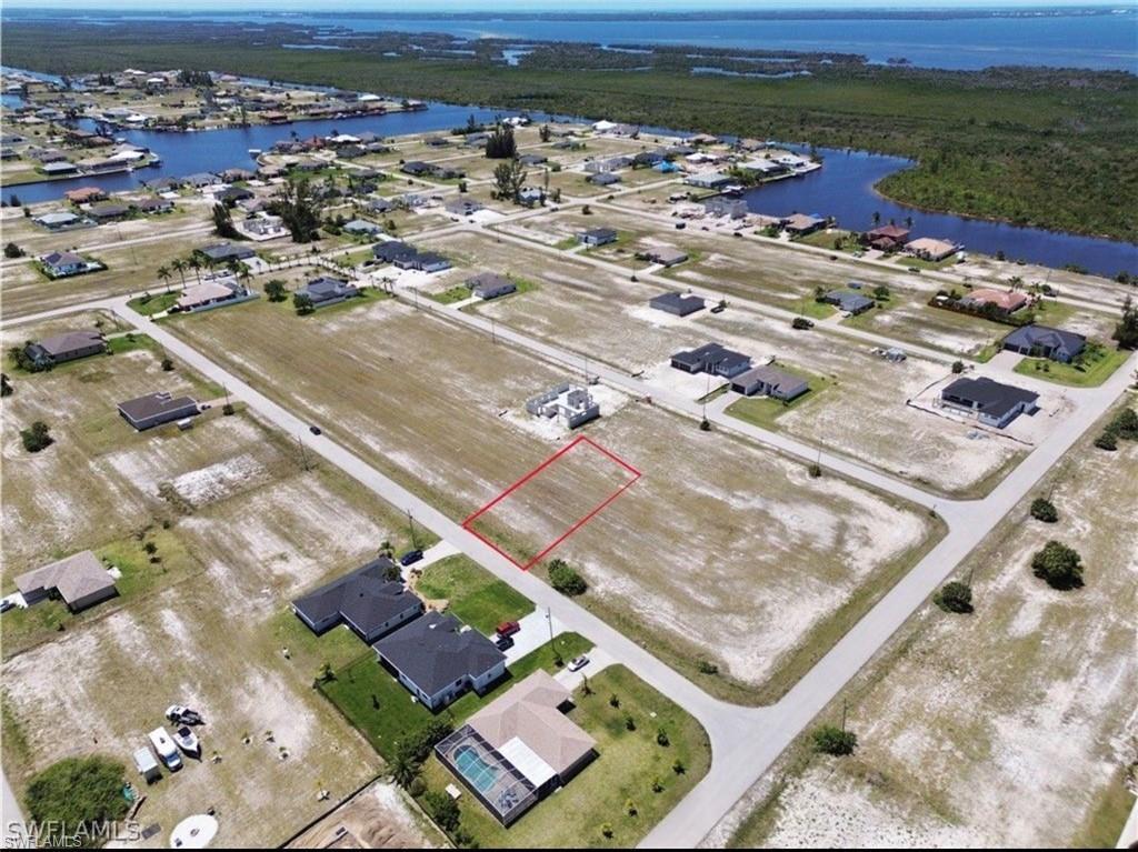 Image 2: Cleared residential lot with street frontage, featuring proximity to existing homes and a backdrop of waterways and undeveloped land